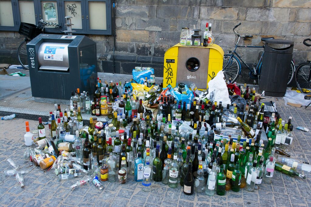 A large pile of glass bottles for recycling on a city street, emphasizing urban waste and recycling.